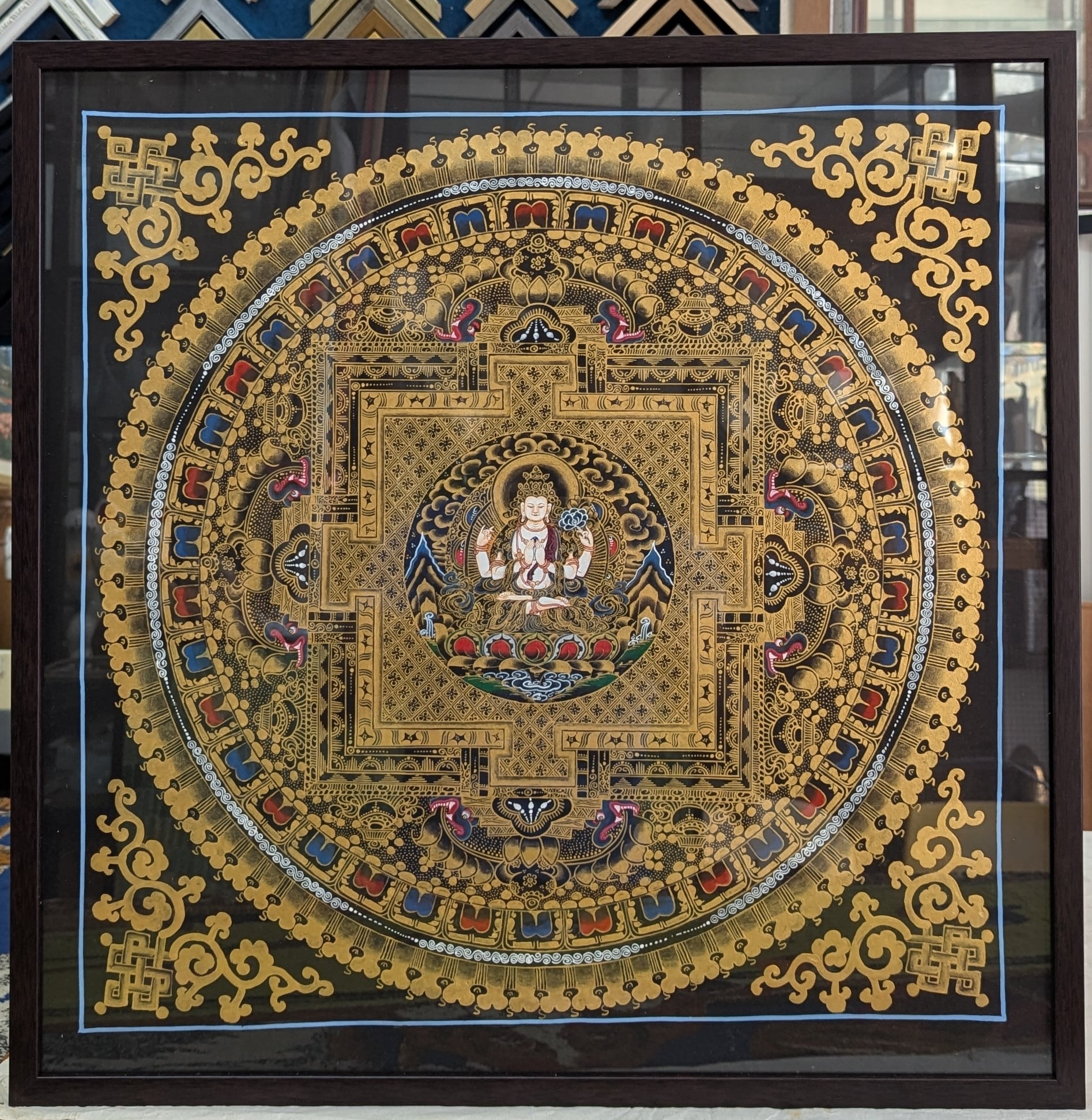 Professional thangka framing with dark brown frame and conservation materials. Traditional presentation for Buddhist religious artwork.